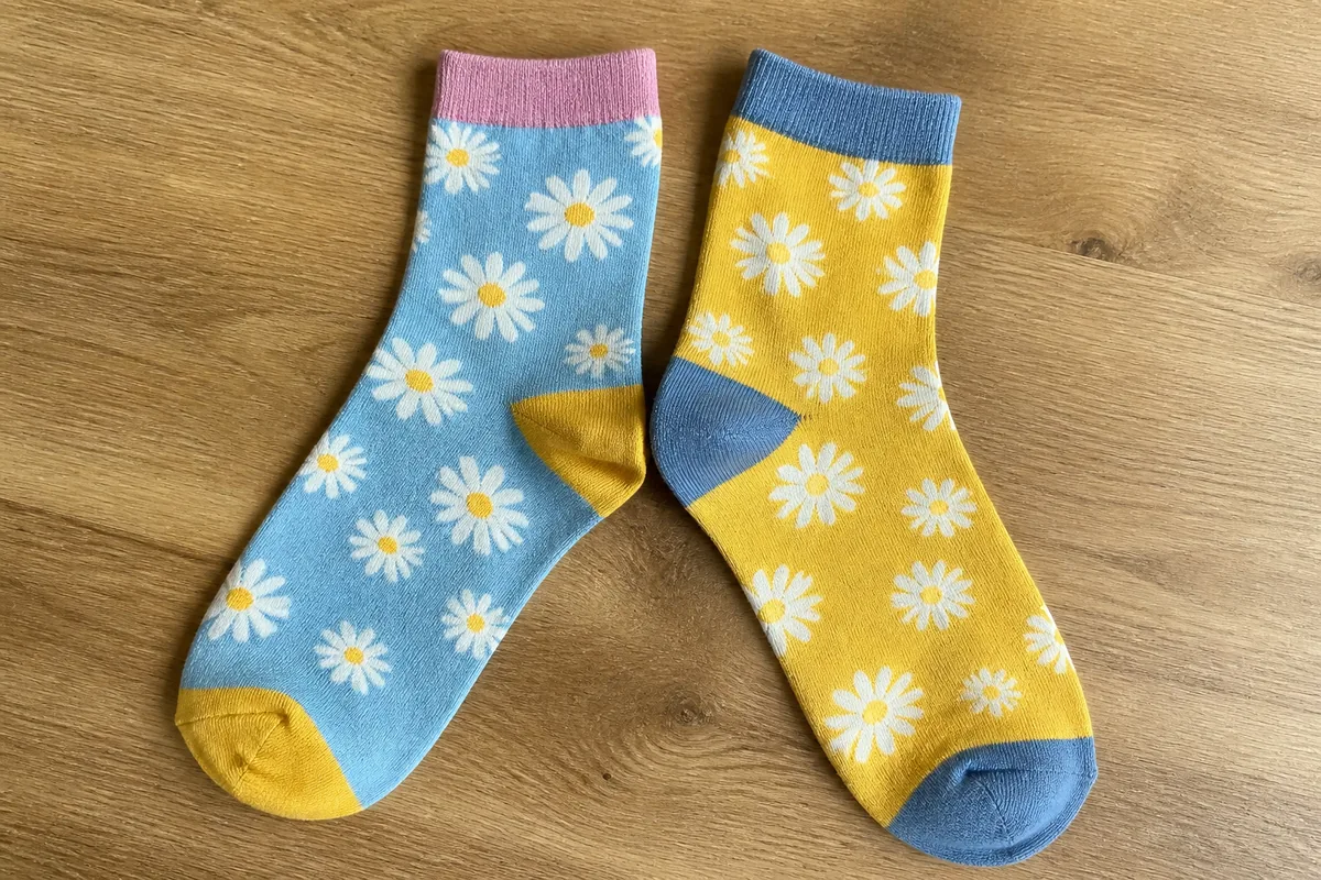 Paire de chaussettes dépareillées colorées avec motifs floraux pâquerettes, posées sur un fond en bois naturel